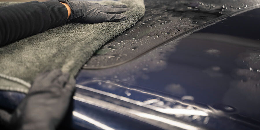 Car wash worker wipes the car after washing with microfiber towel. Professional car wash